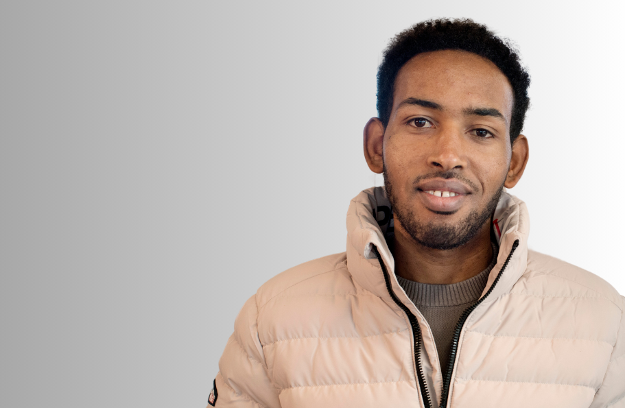 A young man with a pale jacket and a beard. He's smiling.