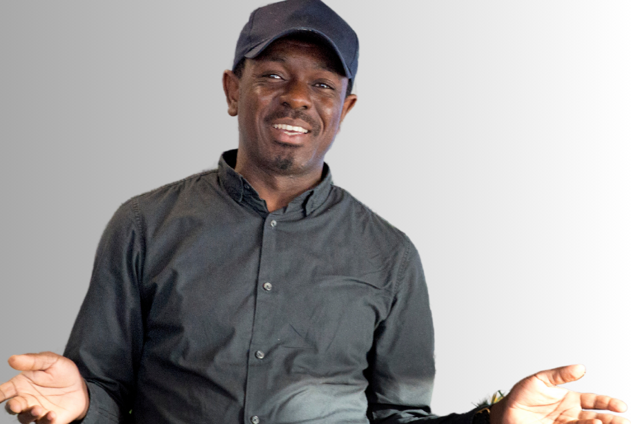 A man in a black shirt and cap, he's of African heritage, and is smiling with his hands open.